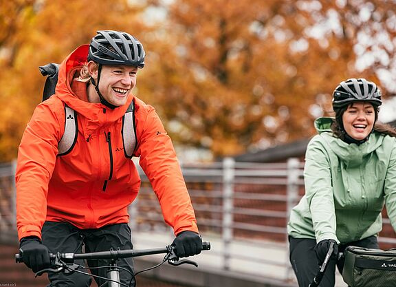 Radfahren im Herbst Eine Frau und ein Mann mit Fahrrädern von vorn in herbstlicher Kleidung lächlen in die Kamera.